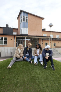 Teenage friends sitting on lawn in front of school
