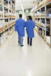 Rear view of technicians walking on aisle in factory