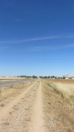 Road amidst field against clear blue sky