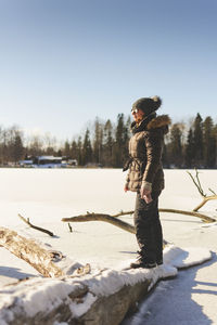 Side view of woman standing on snow field against clear sky during winter