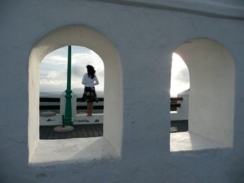 Rear view of woman standing by railing against cloudy sky seen through arch