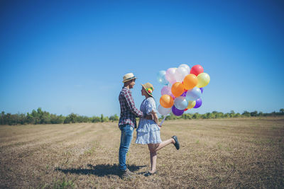 Rear view of people with balloons on field against sky