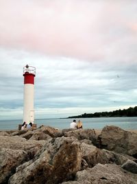 People sitting on rocks by lighthouse at beach