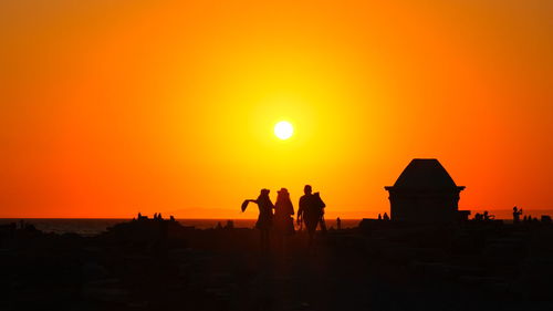 Silhouette people at beach against orange sky