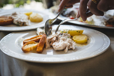 The wise hands of the waiter who puts the fish on it with bruschetta and potatoes