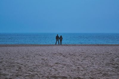 Rear view of silhouette men on beach against clear blue sky