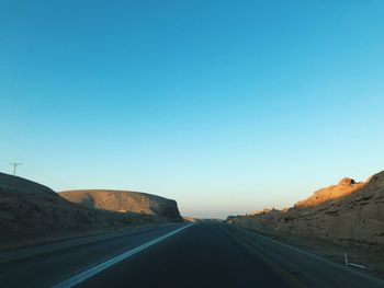 Road at desert against clear blue sky during sunset