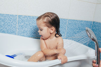 Cropped hand of mother spraying water on daughter in bathroom