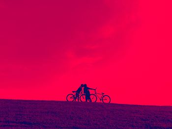 Silhouette person riding bicycle on field during sunset