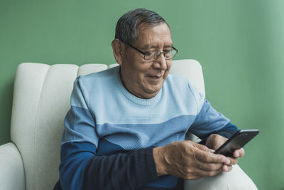 Senior man text messaging on smart phone in front of wall