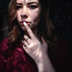 Close-up portrait of young woman touching lips in darkroom