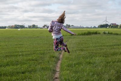 Rear view of girl jumping on field against sky