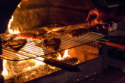 Cropped image of person hand cooking meat on barbecue grill