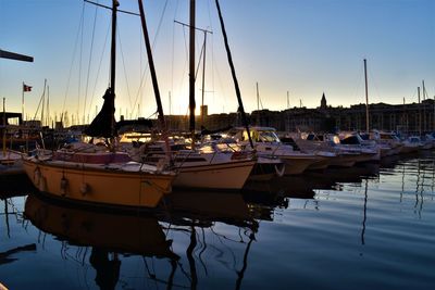 Sailboats moored in harbor at sunset