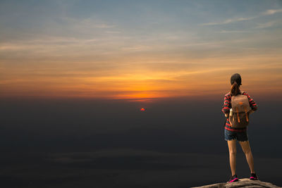 Rear view of woman standing by sea against sky during sunset
