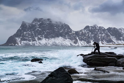 Man photographing sea while standing on rock during winter