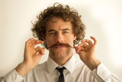 Portrait of confident businessman rolling mustache against white background