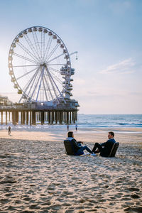 People at amusement park by sea against sky