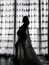 Rear view of pregnant woman standing against window