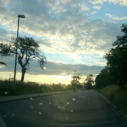 Road by trees against sky at sunset