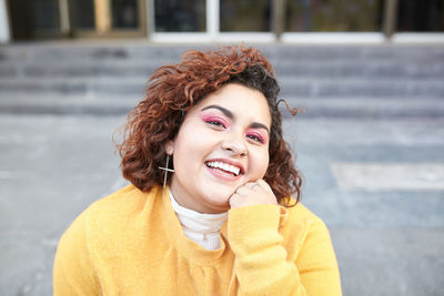 Content plus size female in casual wear sitting on stairs in city and looking at camera while enjoying sunny weather at weekend and touching curly hair