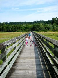 Full length of girl with sister and baby carriage standing amidst field on boardwalk