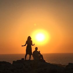 Silhouette people on rock against sea during sunset