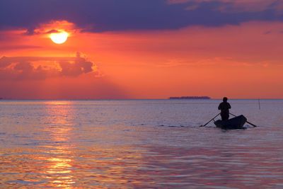 Silhouette man in sea against sky during sunset