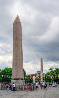 Group of people in front of historical building against cloudy sky