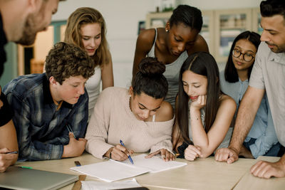 Female studying with friends while professor assisting in classroom