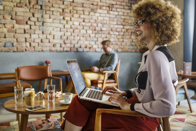 Side view of happy businesswoman looking away while using laptop at hotel lobby