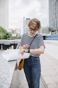 Businesswoman using smart watch standing near wall in city