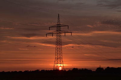 Low angle view of silhouette electricity pylon against sky during sunset