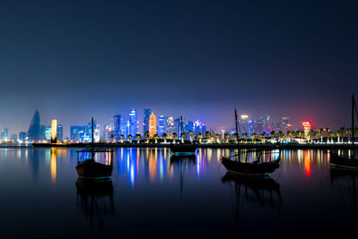 Illuminated buildings by river against sky at night