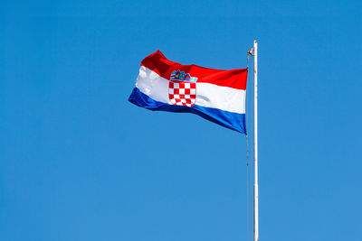 Low angle view of flags against clear blue sky