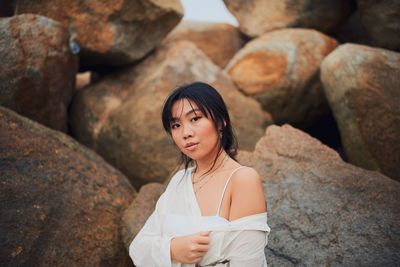 Portrait of young woman standing by rock formation