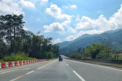 Empty road by trees against sky