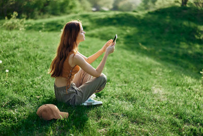 Young woman using mobile phone while sitting on grassy field