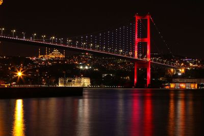 Illuminated bridge over river against sky at night