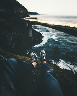 Low section of man relaxing on cliff against sea