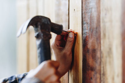 Cropped hands hammering nail in wooden wall