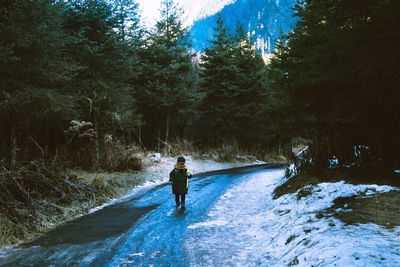 Boy walking on road in forest during winter