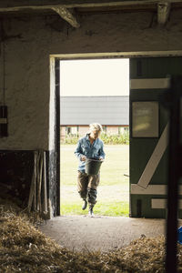 Woman holding bucket entering barn at farm