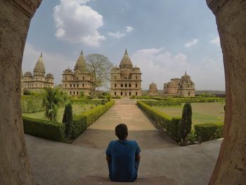 Rear view of man outside building against sky