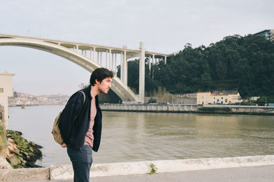 Man looking away while standing against bridge