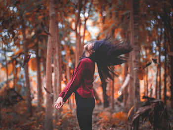 Midsection of woman standing by trees in forest during autumn