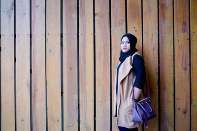 Portrait of woman standing against wooden wall