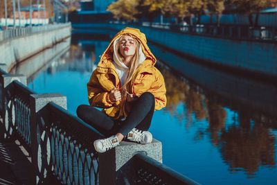 Woman sitting on railing by canal during winter