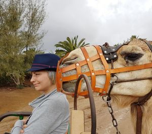 Side view of woman sitting by camel wearing muzzle