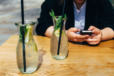 Midsection of woman using phone while sitting by drinks served on table